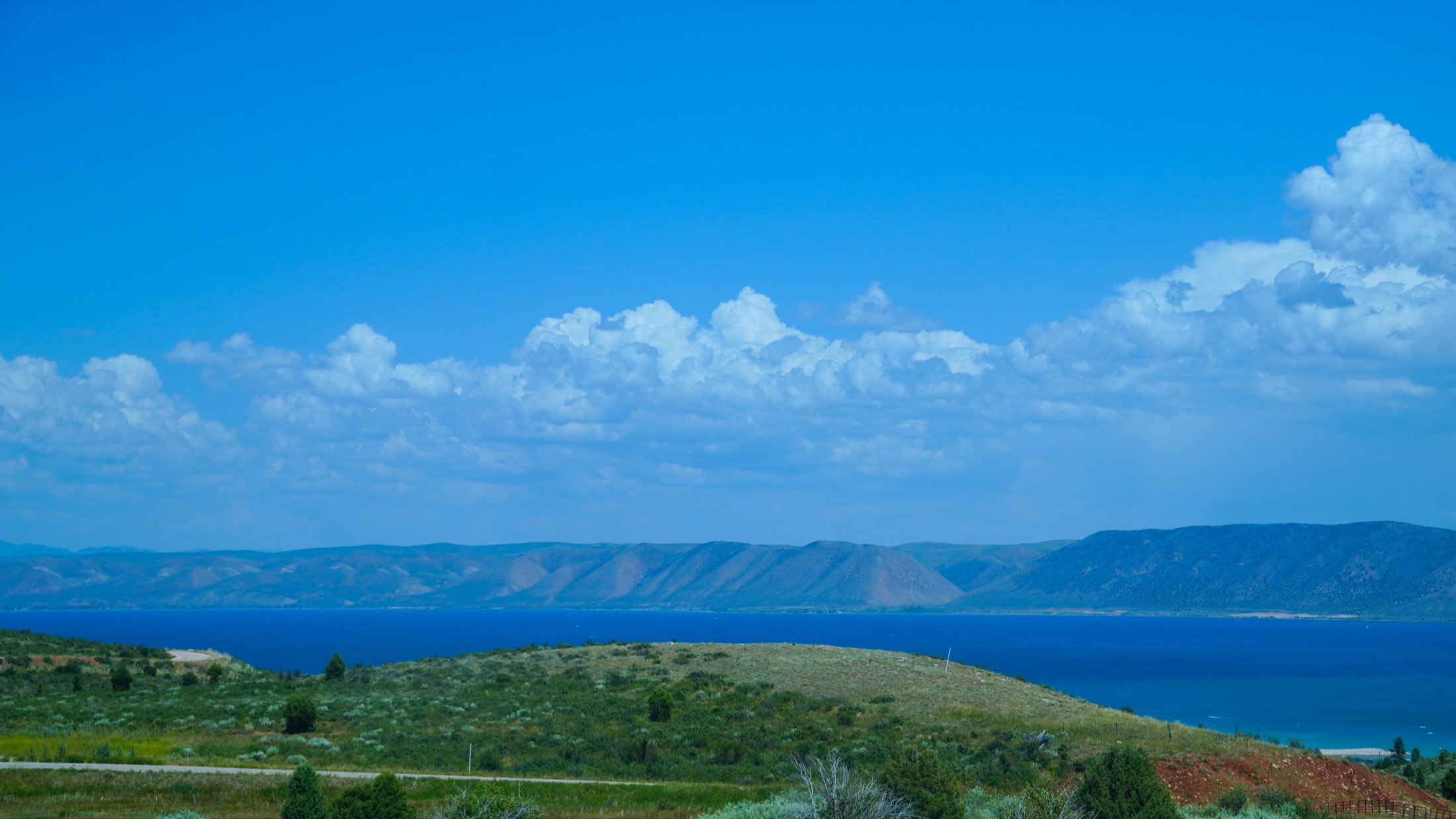 A broad blue lake stretching toward distant cliffs under summer clouds