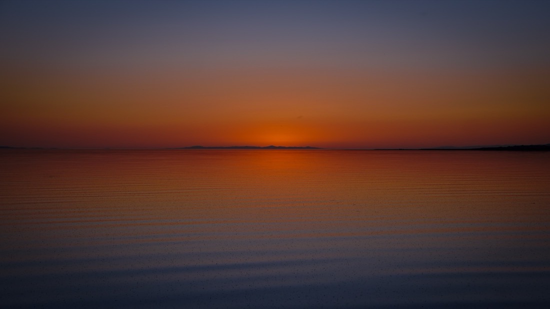 The sun setting over still water